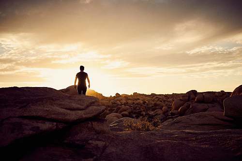 rock man walking on gray rocks under yellow sky during daytime sunrise